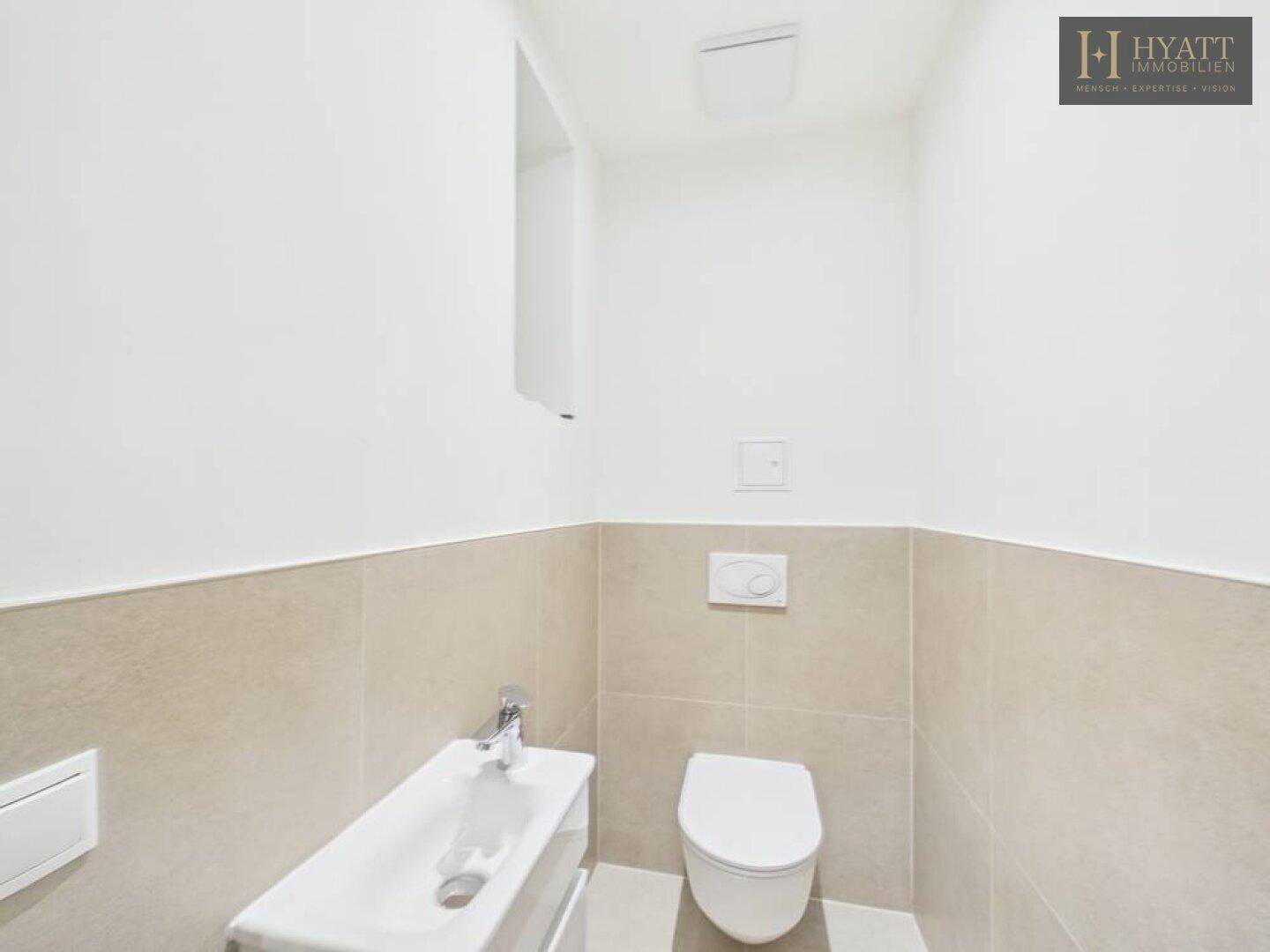 Modernes Gäste-WC mit Wand-WC, kleinem Waschbecken und hellen Fliesen.