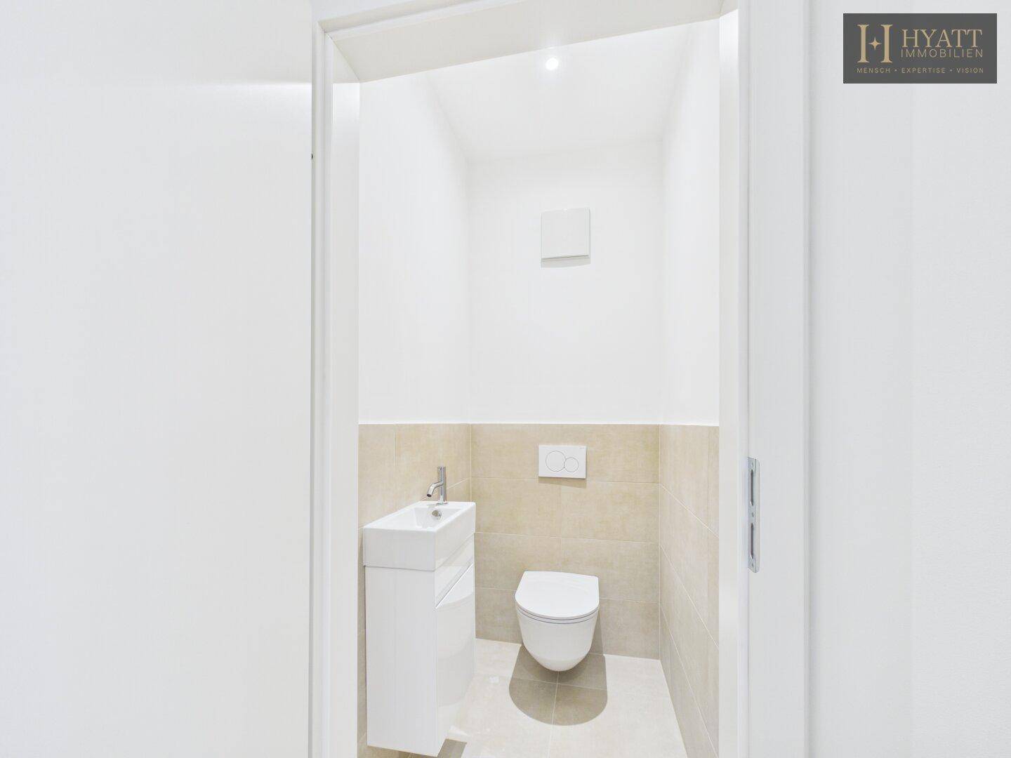 Modernes Gäste-WC mit wandhängender Toilette und kleinem Waschbecken, hell gefliest.
