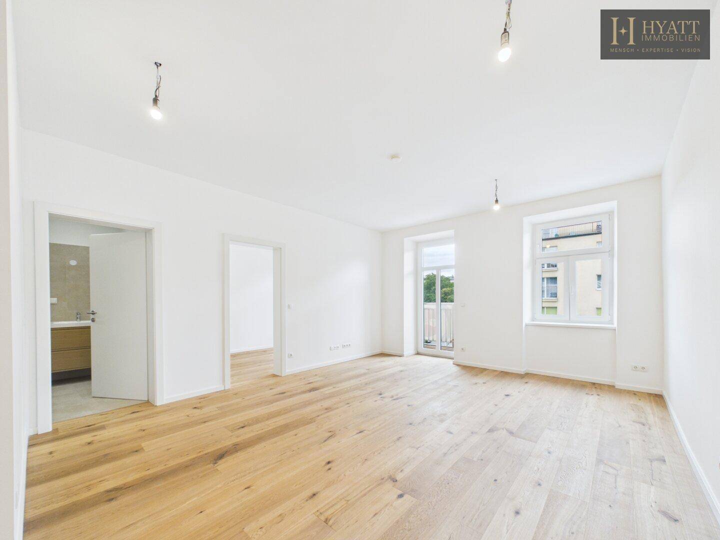 Geräumiges, helles Zimmer mit Holzboden und Zugang zu einem Balkon, angrenzend an ein Badezimmer.