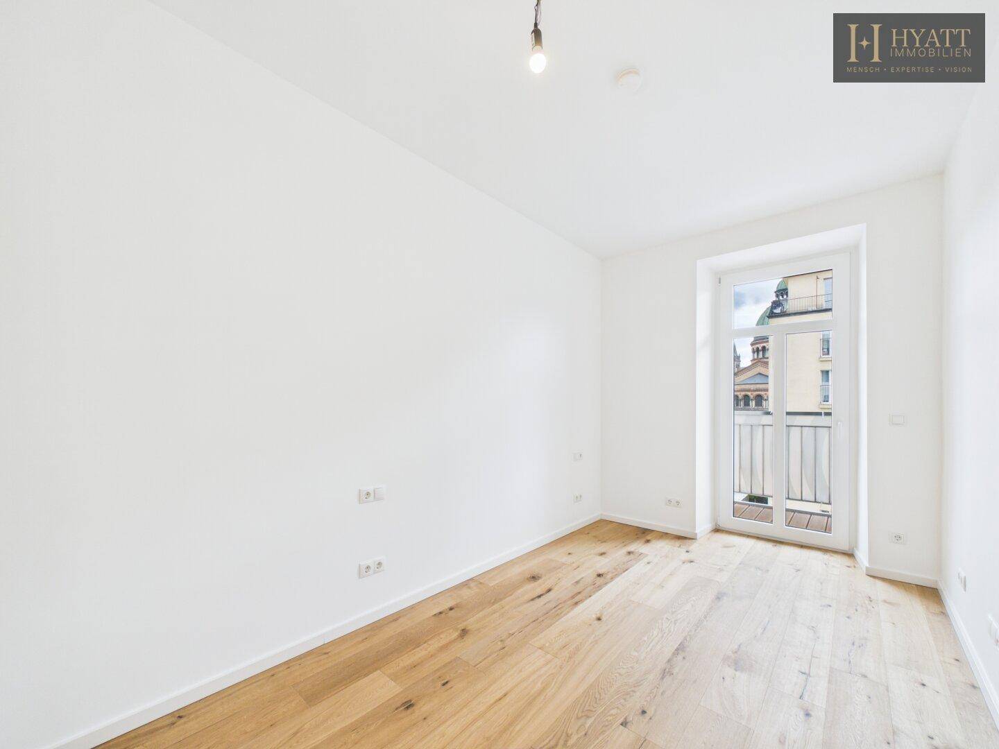 Helles Schlafzimmer mit Holzboden und einem französischen Balkon, bietet viel Tageslicht.