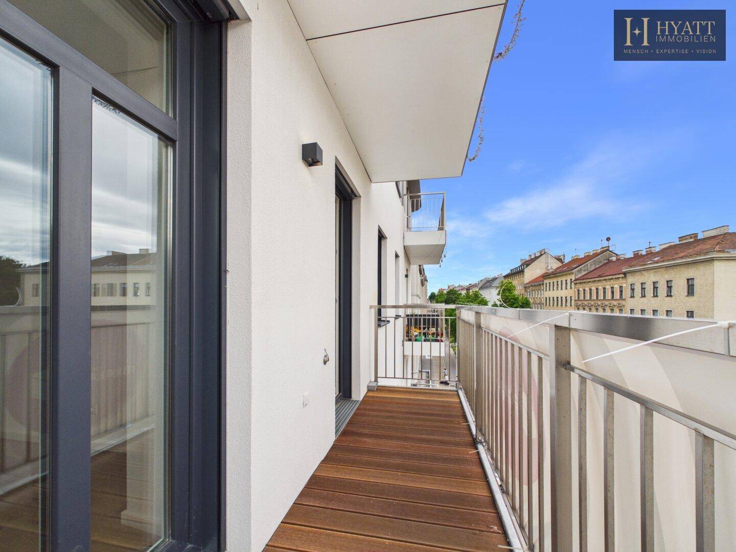 Langer Balkon mit Holzdielen und moderner Metallbrüstung, bietet einen weiten Stadtblick.