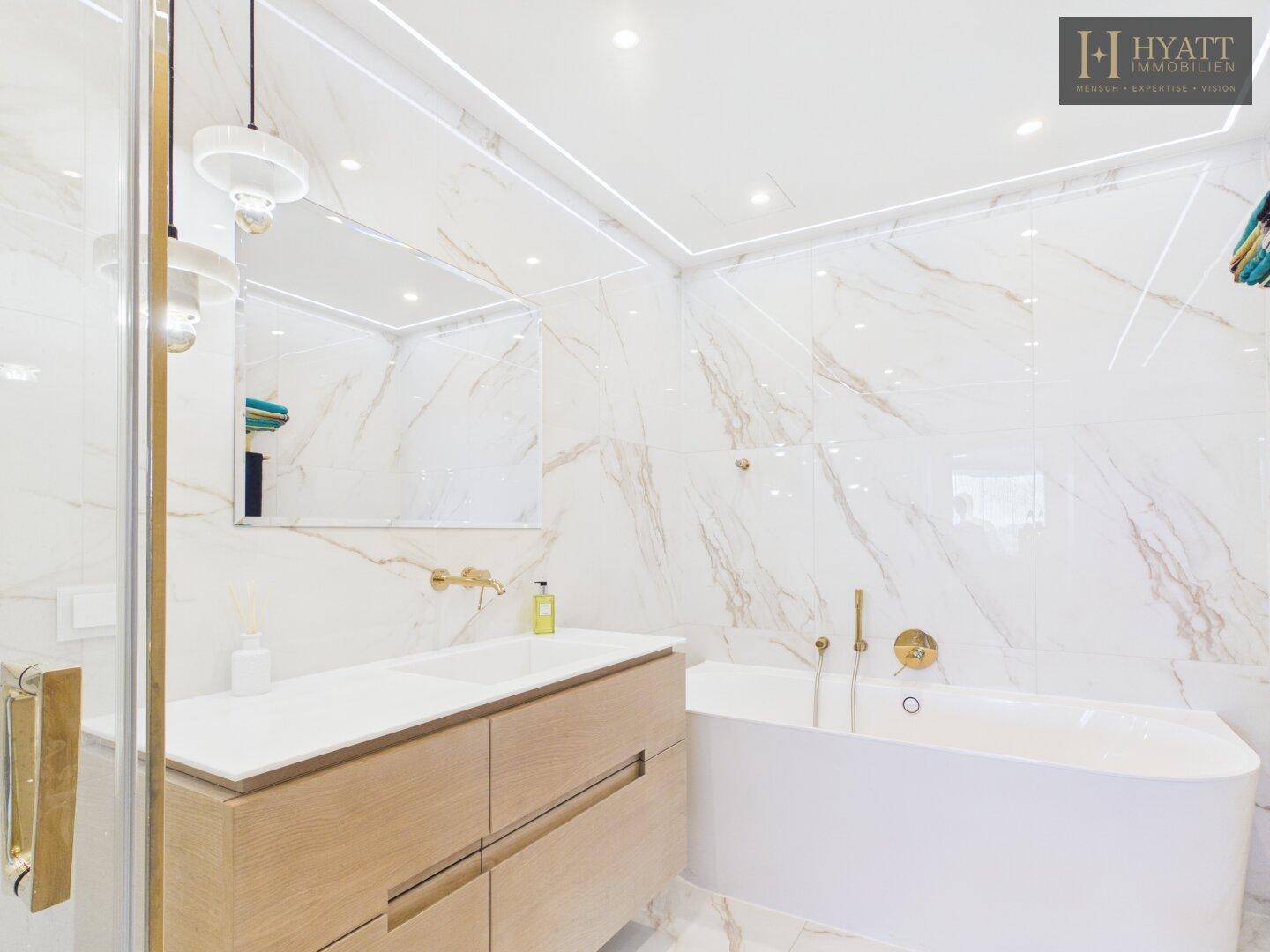 Elegantes Badezimmer mit Marmorfliesen, Doppelwaschbecken, freistehender Badewanne und goldenen Armaturen.