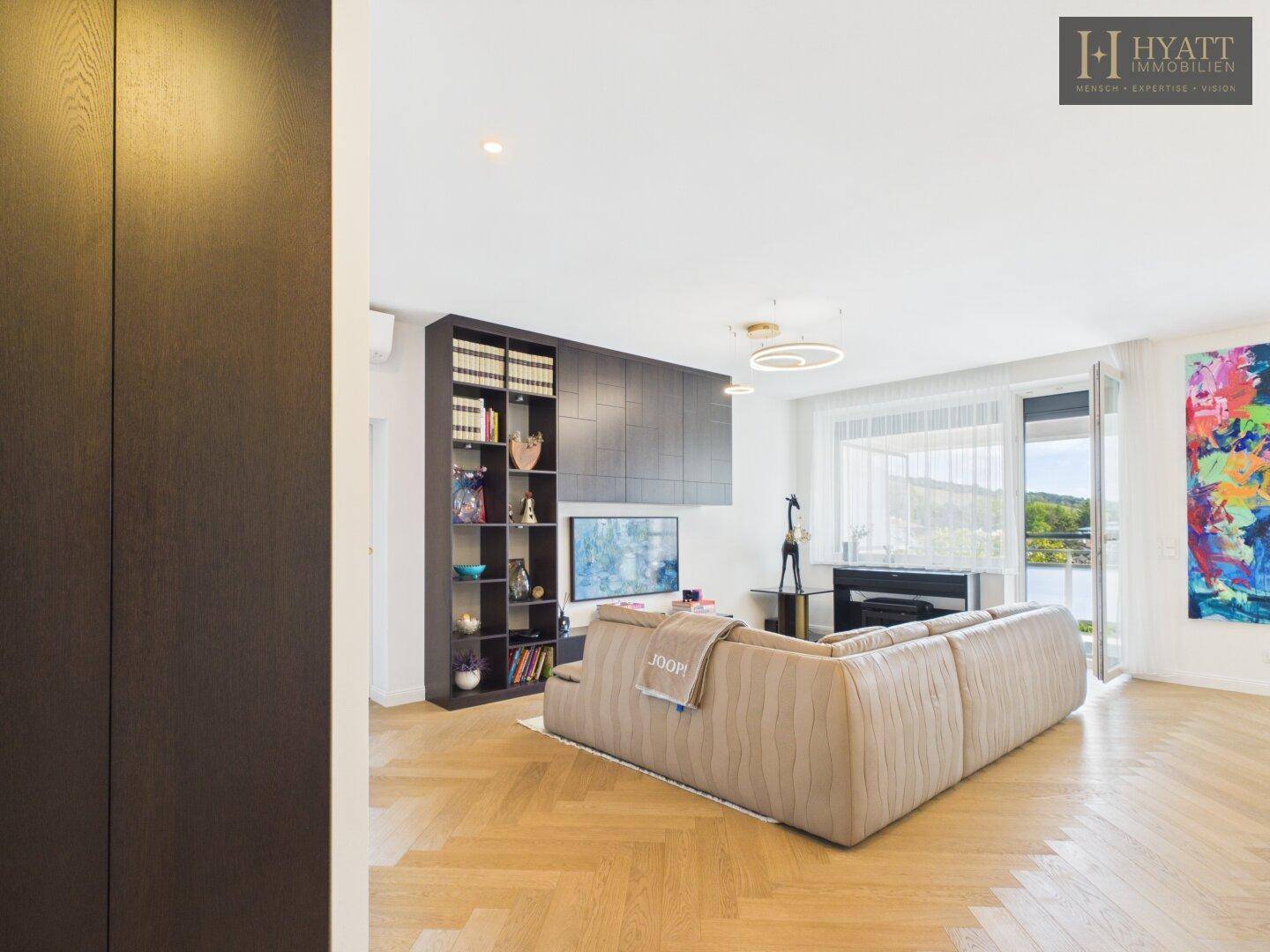 Gemütliches Wohnzimmer mit großem Sofa, Einbauregal und Zugang zu einem Balkon mit Weitblick.