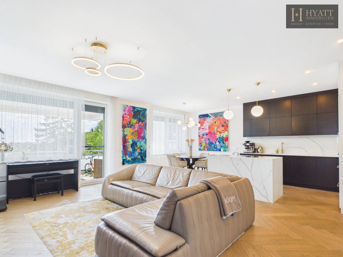 Heller offener Wohn-Essbereich mit integrierter Küche, großem Sofa und Zugang zum Balkon.