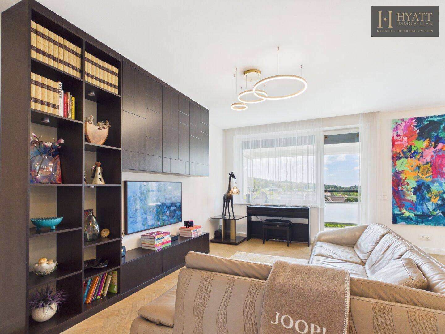 Geräumiges Wohnzimmer mit modernem Sofa, Einbauregal und großen Fenstern mit Blick ins Grüne.