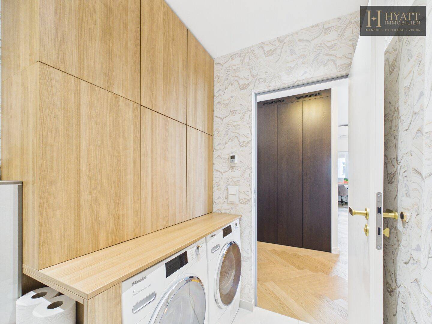 Praktischer Hauswirtschaftsraum mit Waschmaschine, Trockner und maßgefertigten Holzschränken.
