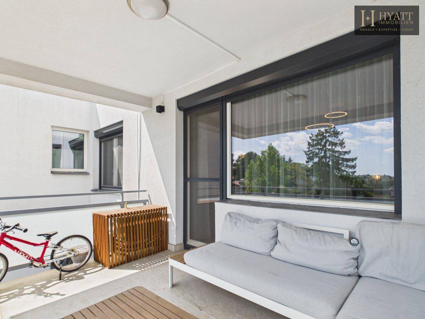 Gemütlicher Balkon mit Sitzgelegenheiten, Fahrrad und Blick auf die grüne Umgebung.