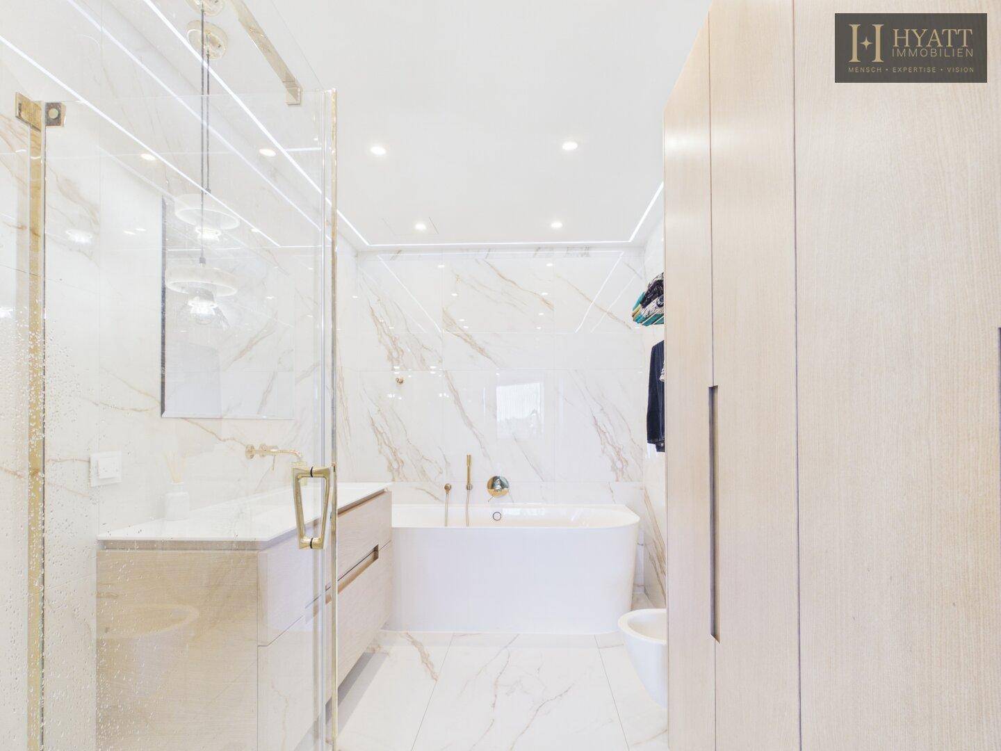 Geräumiges Badezimmer mit Marmorfliesen, Badewanne und praktischen Holzschränken.