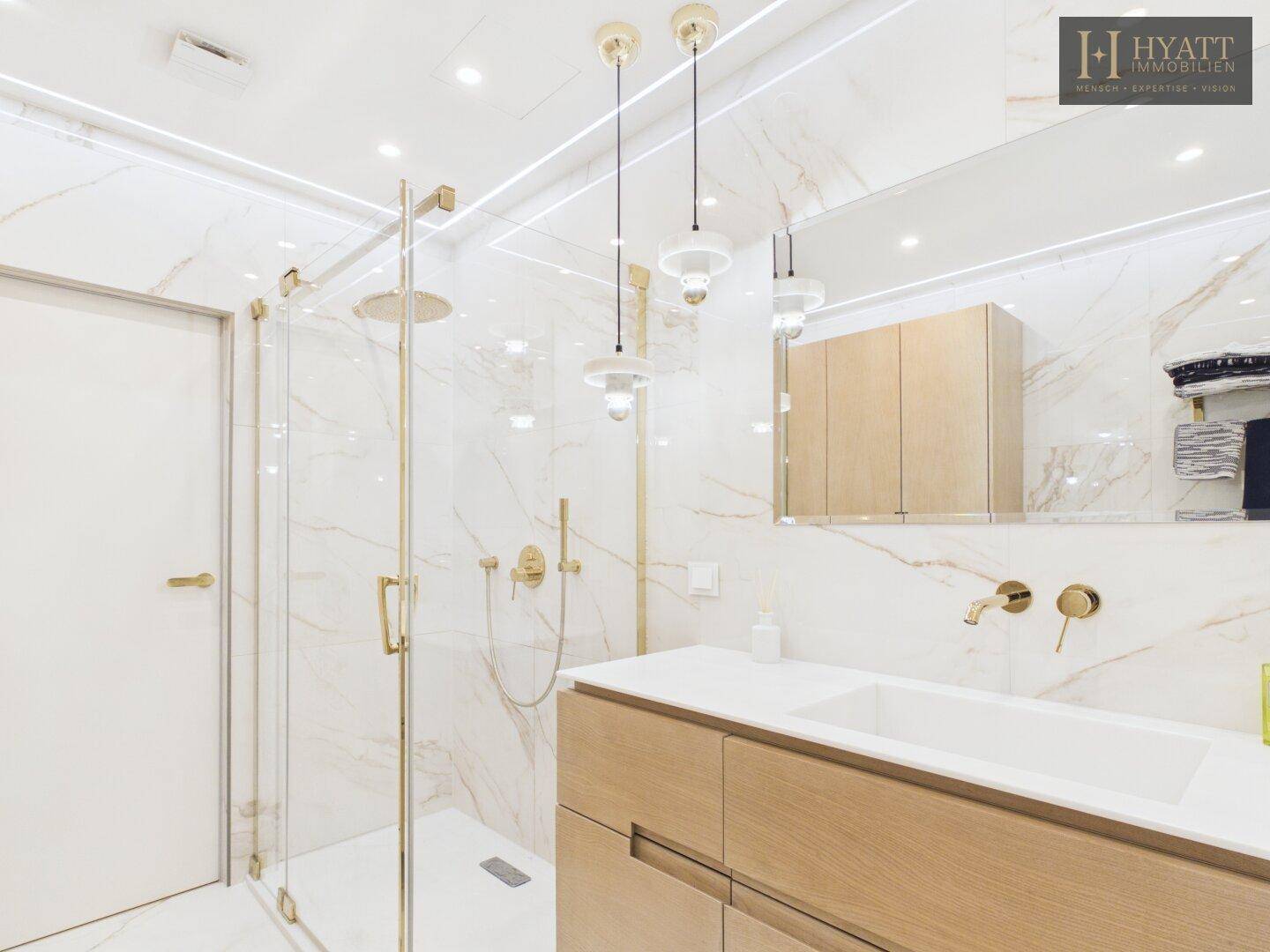 Modernes Badezimmer mit Marmorfliesen, begehbarer Dusche und eleganten goldenen Armaturen.