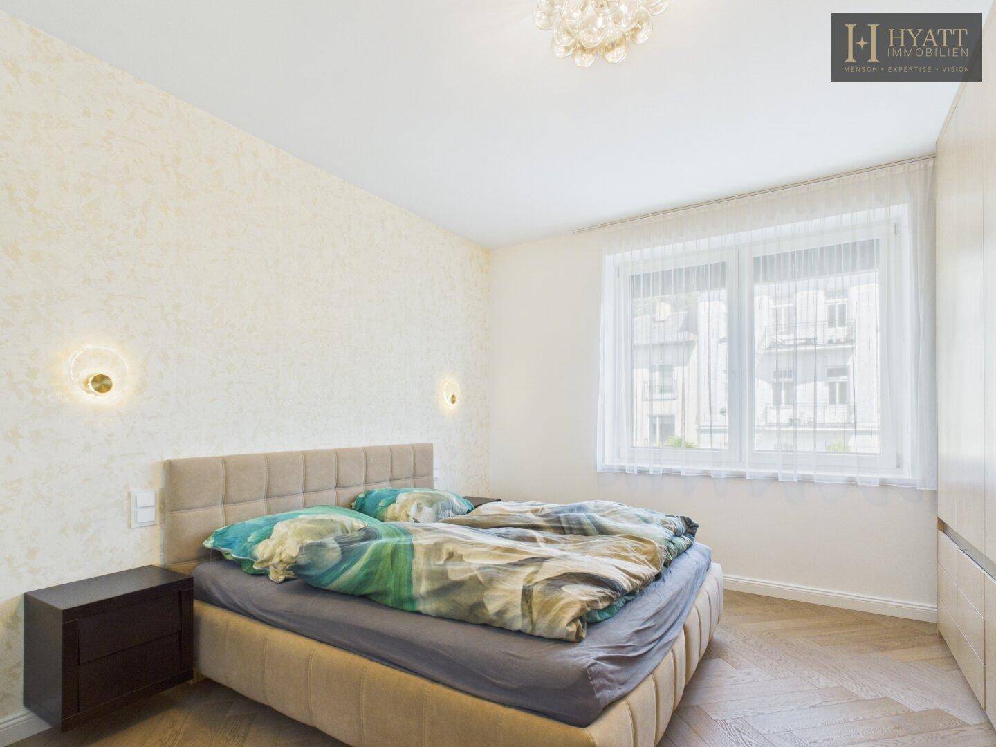 Helles Schlafzimmer mit komfortablem Bett, Nachttisch und Fenster, das viel Tageslicht hereinlässt.