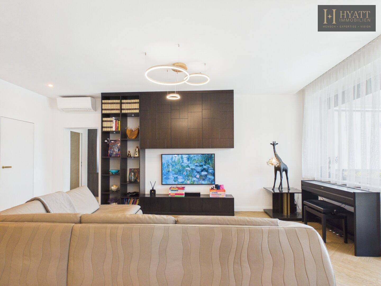 Geräumiges Wohnzimmer mit beigem Sofa, Fernseher und stilvollen dunklen Einbaumöbeln.