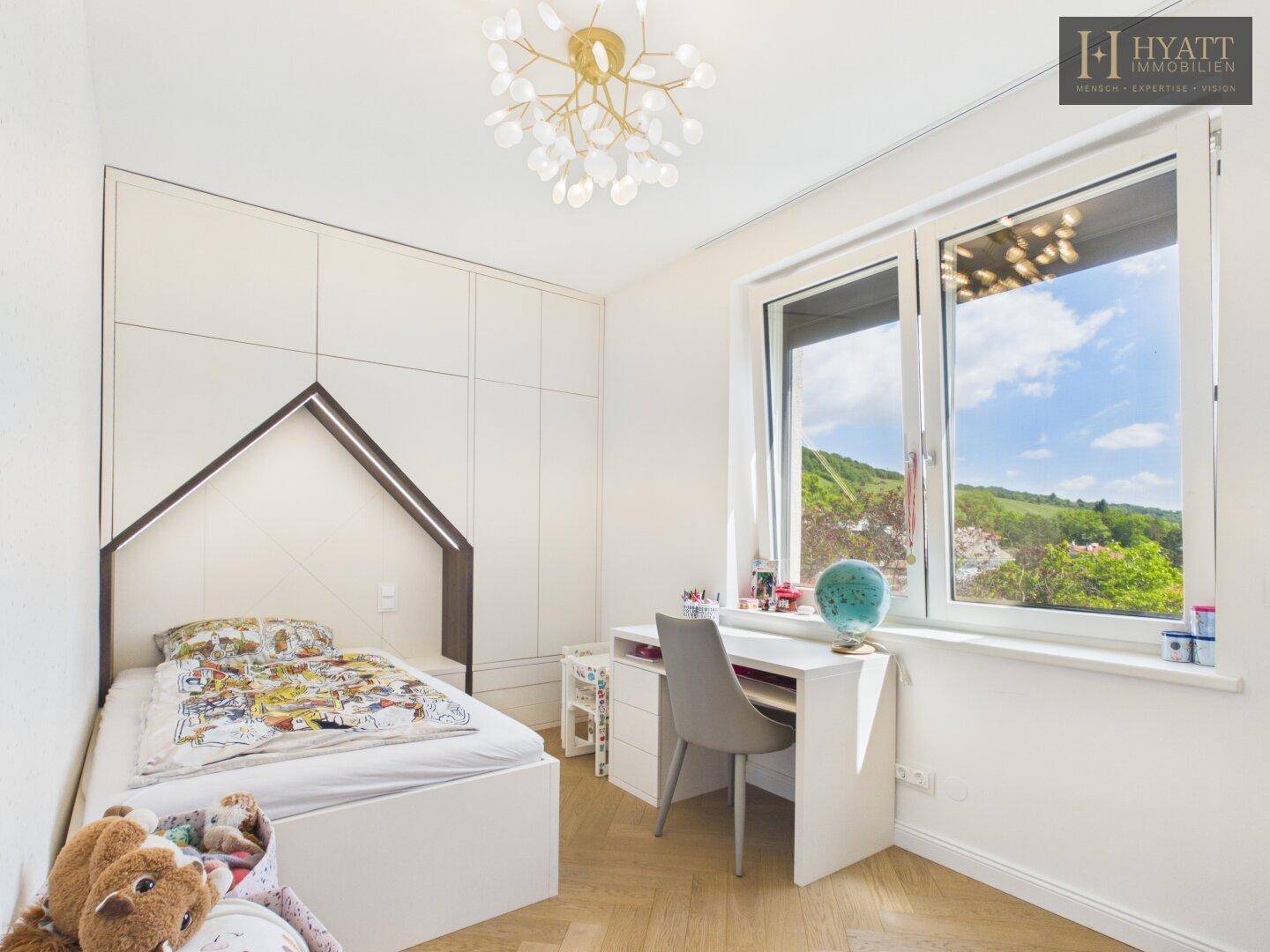 Kinderzimmer mit Einzelbett, Schreibtisch und großem Fenster mit Blick ins Grüne.