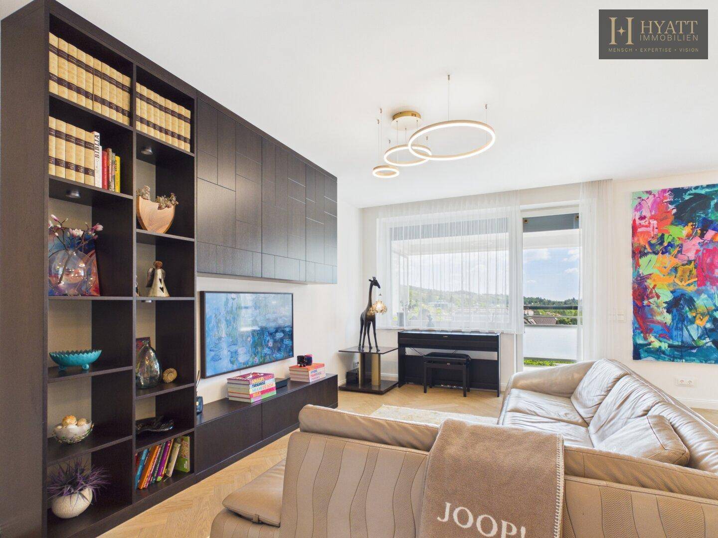 Großzügiges Wohnzimmer mit Sofa, Bücherregal und Blick auf die grüne Landschaft.