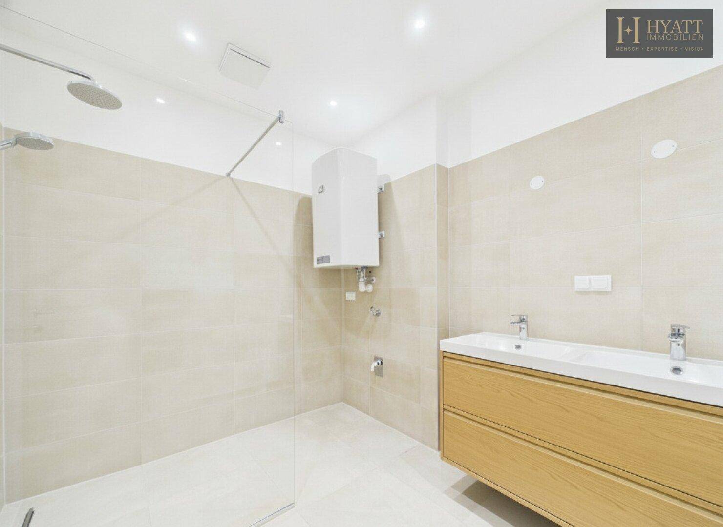 Modernes Badezimmer mit begehbarer Dusche, Doppelwaschbecken und hellen Fliesen in neuwertigem Zustand.