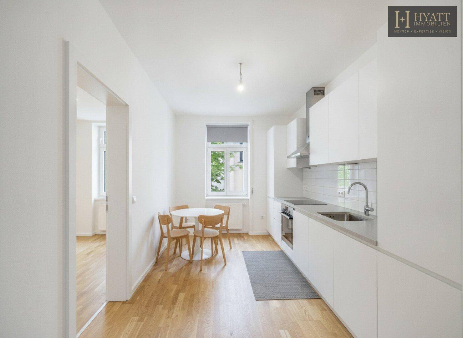 Moderne Küche mit weißen Schränken, integrierten Geräten und kleinem Essbereich am Fenster.