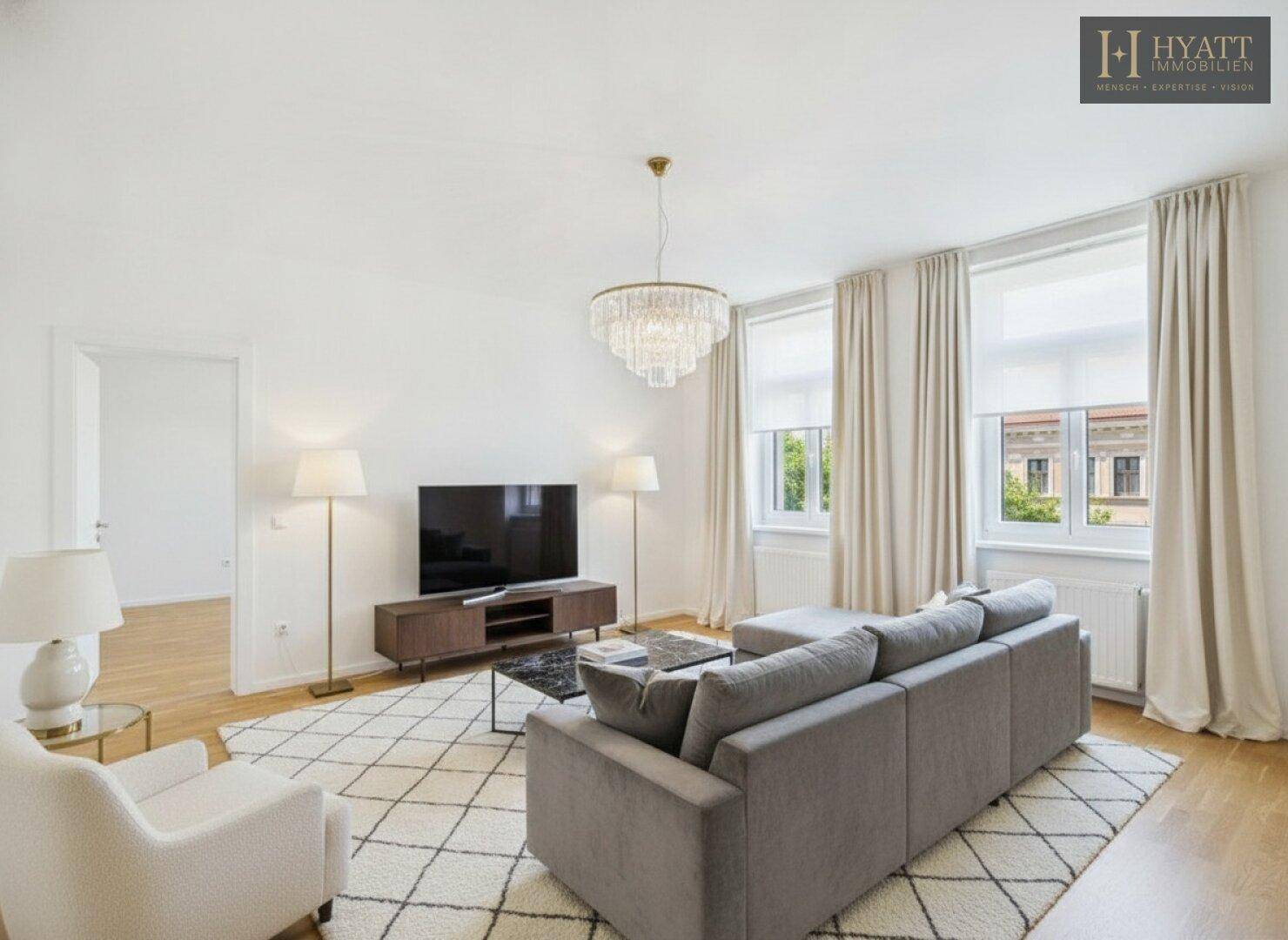 Geräumiges Wohnzimmer mit grauem Sofa, Fernseher, Holzboden und elegantem Kronleuchter.