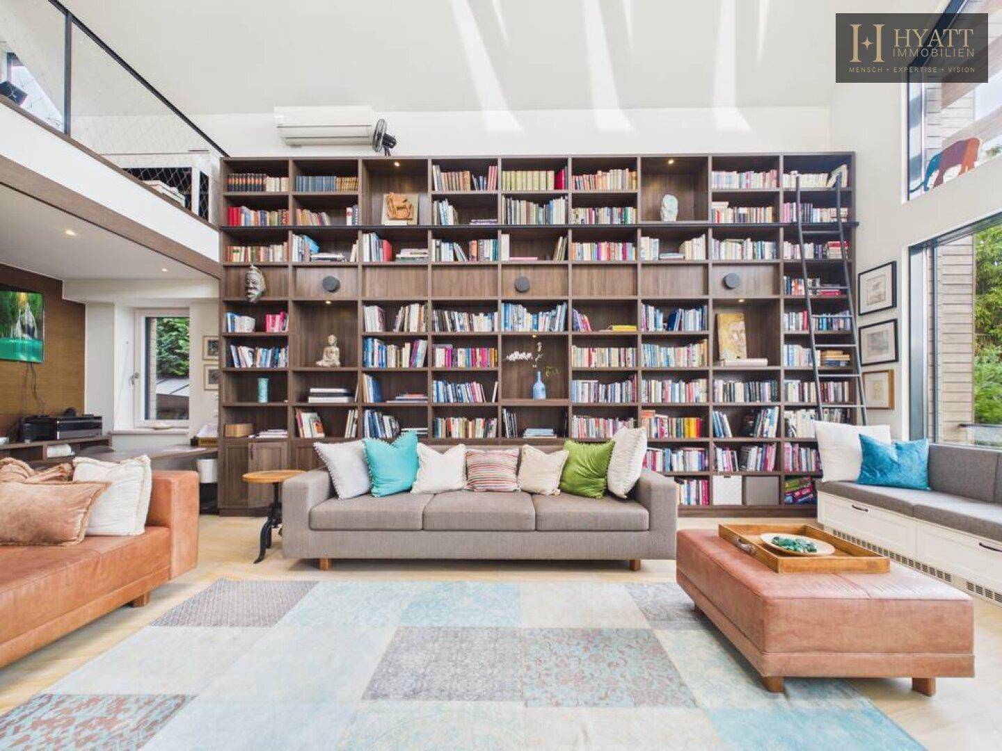 Heller Wohnbereich mit beeindruckender Bücherwand, bequemen Sofas und Zugang zur Galerie.