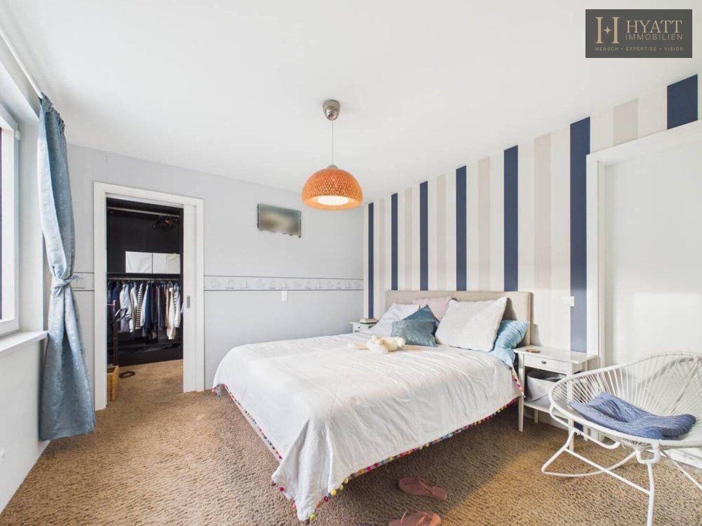Schlafzimmer mit Doppelbett, gestreifter Tapete und direktem Zugang zum begehbaren Kleiderschrank.