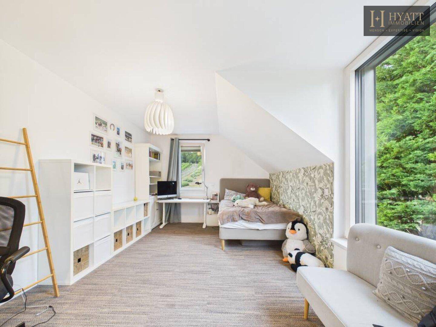 Kinderzimmer mit Bett, Schreibtisch, Regalen und großem Fenster mit Blick ins Grüne.