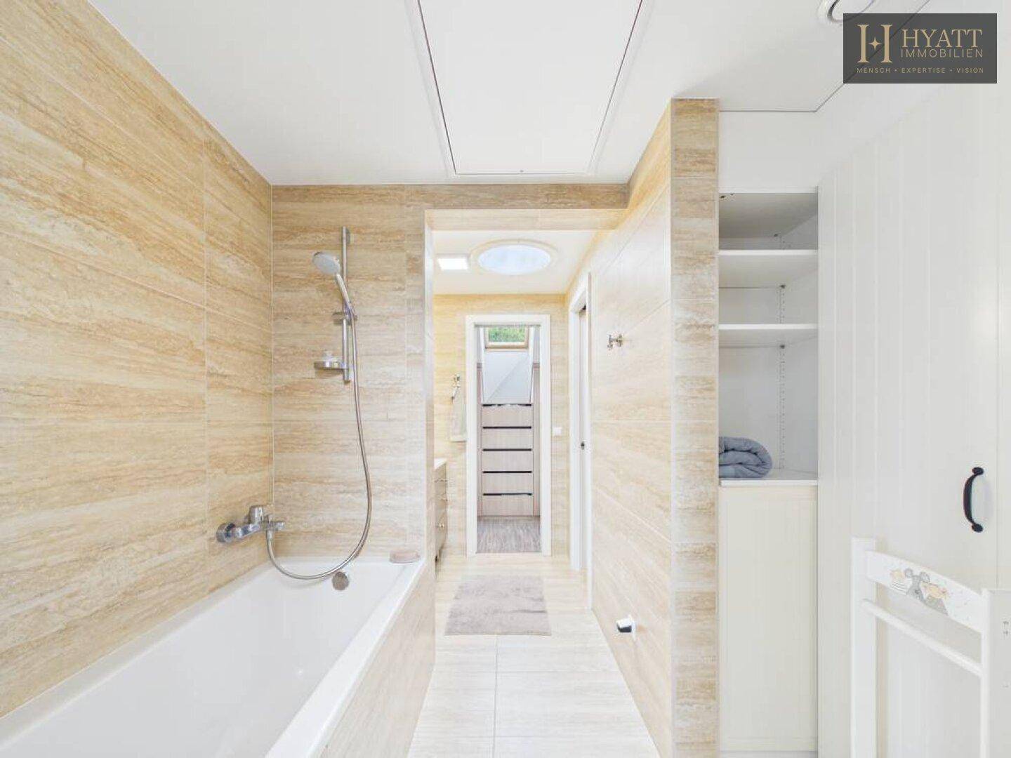 Modernes Badezimmer mit Badewanne, hellen Fliesen und Zugang zu einem weiteren Raum.