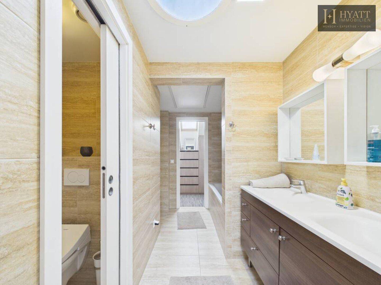 Geräumiges Badezimmer mit Doppelwaschbecken, WC und natürlichem Licht durch Oberlicht.