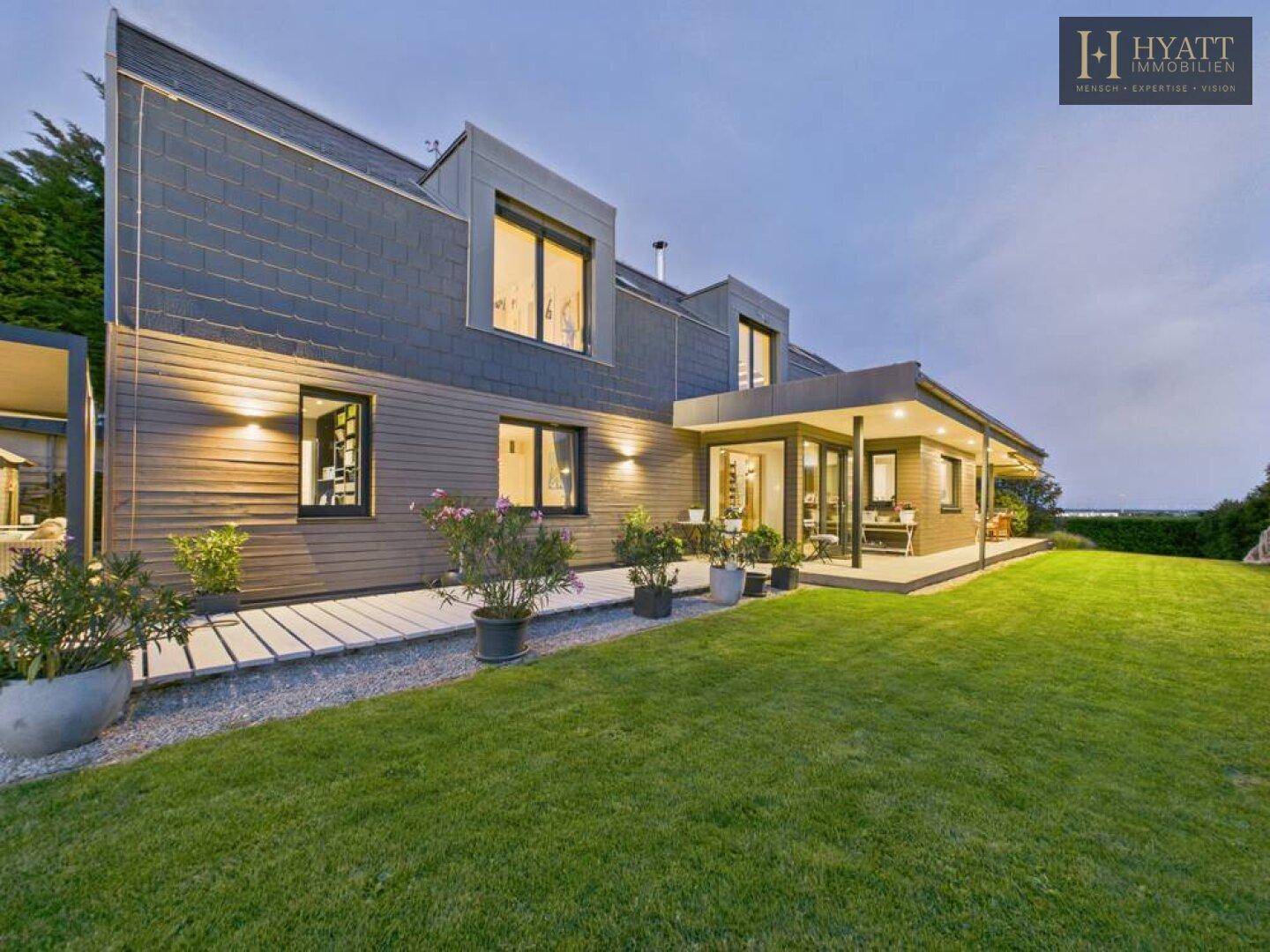 Rückseite des modernen Hauses mit gepflegtem Rasen und Terrasse am Abend.