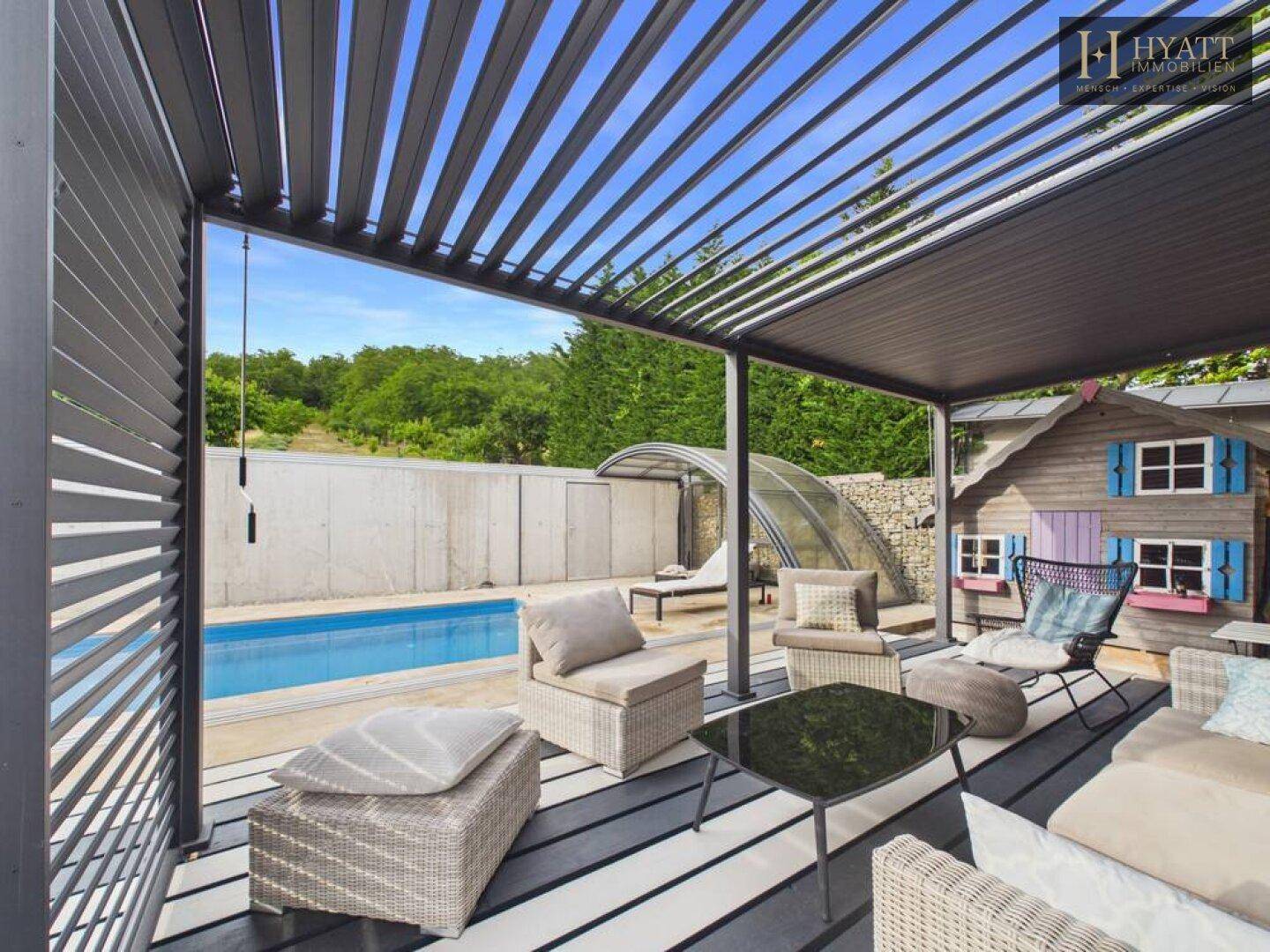 Überdachte Terrasse mit Lounge-Möbeln, Blick auf den Pool und ein charmantes Spielhaus.