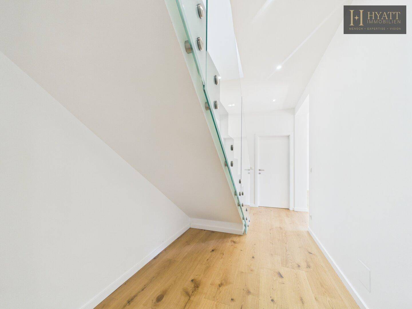 Heller Flur mit Eichenparkett und modernem Glasgeländer unter der Treppe.