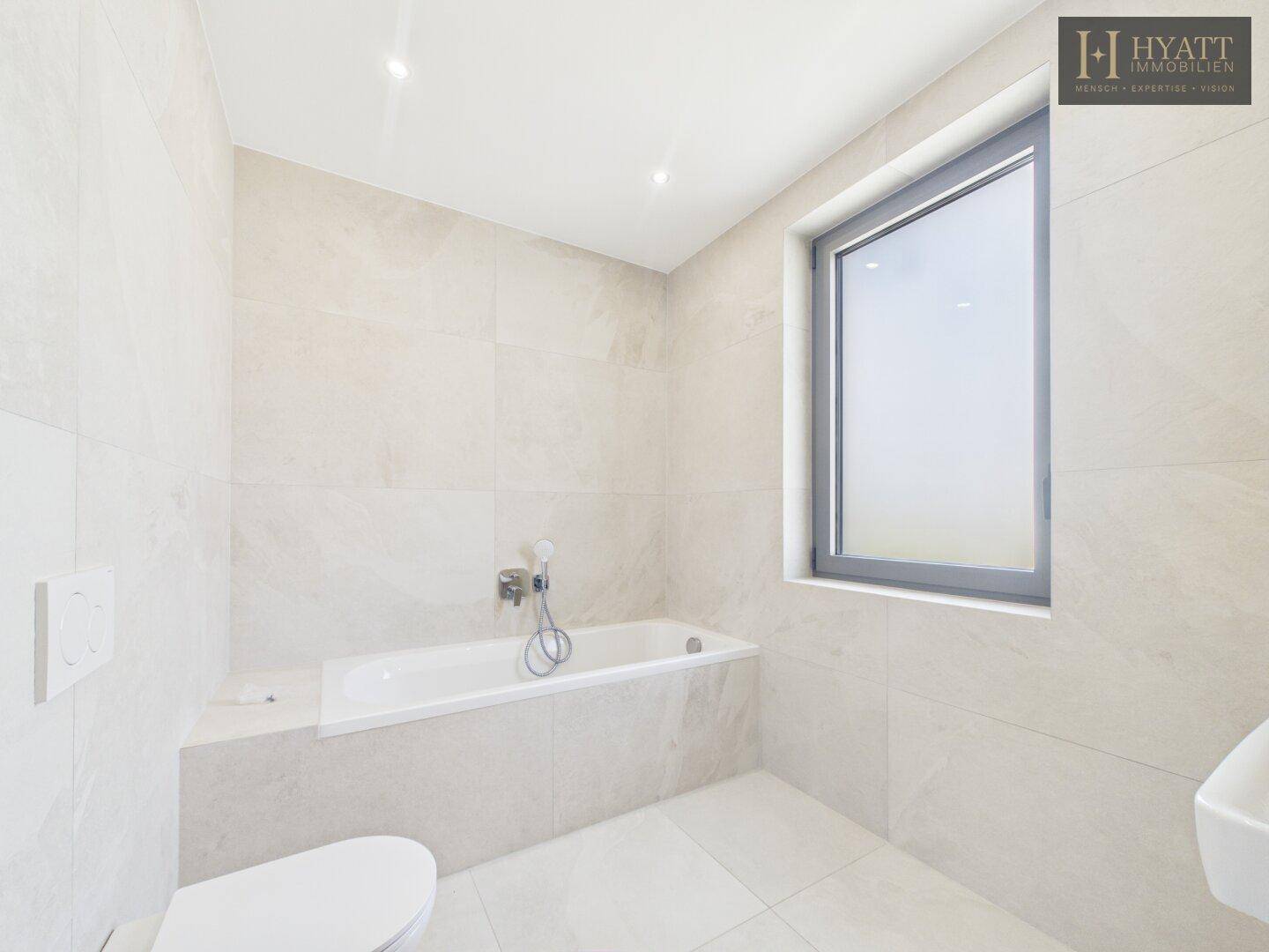 Modernes Badezimmer mit Badewanne, Wand-WC, Waschbecken und Fenster.