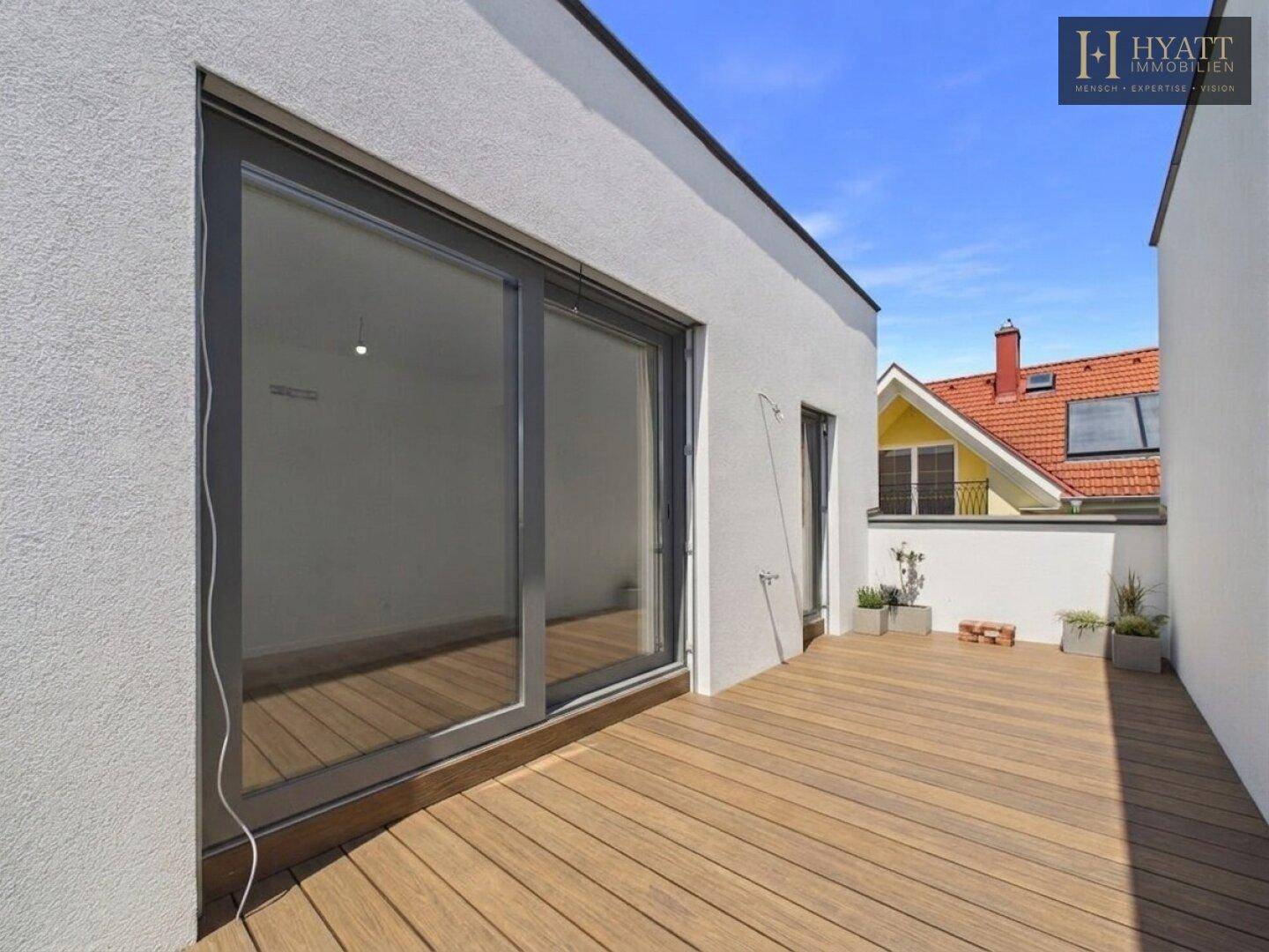Sonniger Balkon mit Holzdielen und Ausblick auf die umliegenden Dächer.