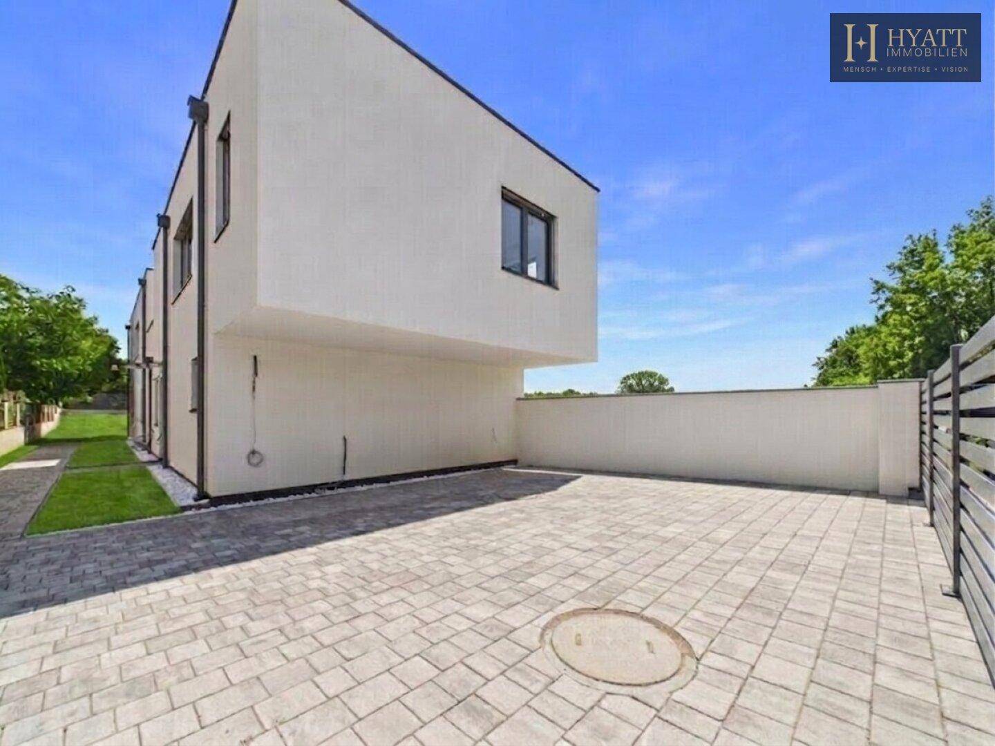 Moderne Architektur mit weißer Fassade und gepflastertem Vorplatz unter blauem Himmel.