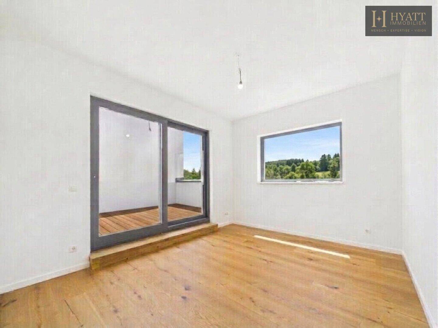 Geräumiges Schlafzimmer mit Holzboden, Fenster und Schiebetür zum Balkon mit Aussicht.