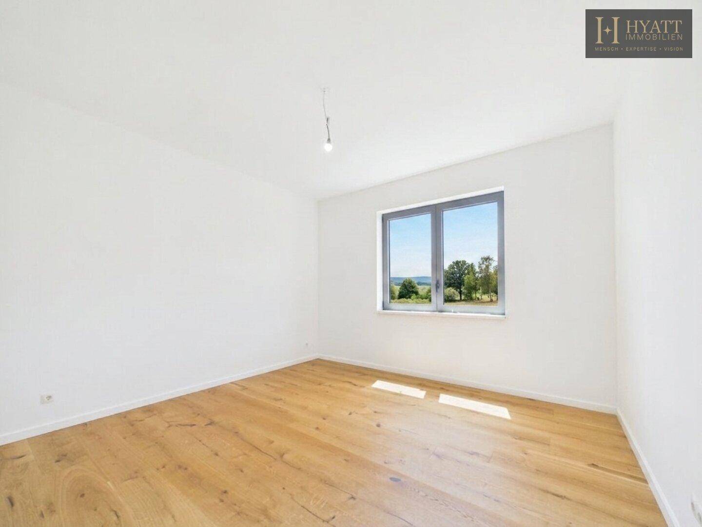 Helles Schlafzimmer mit Holzboden und Fenster, das einen weiten Blick in die Landschaft bietet.