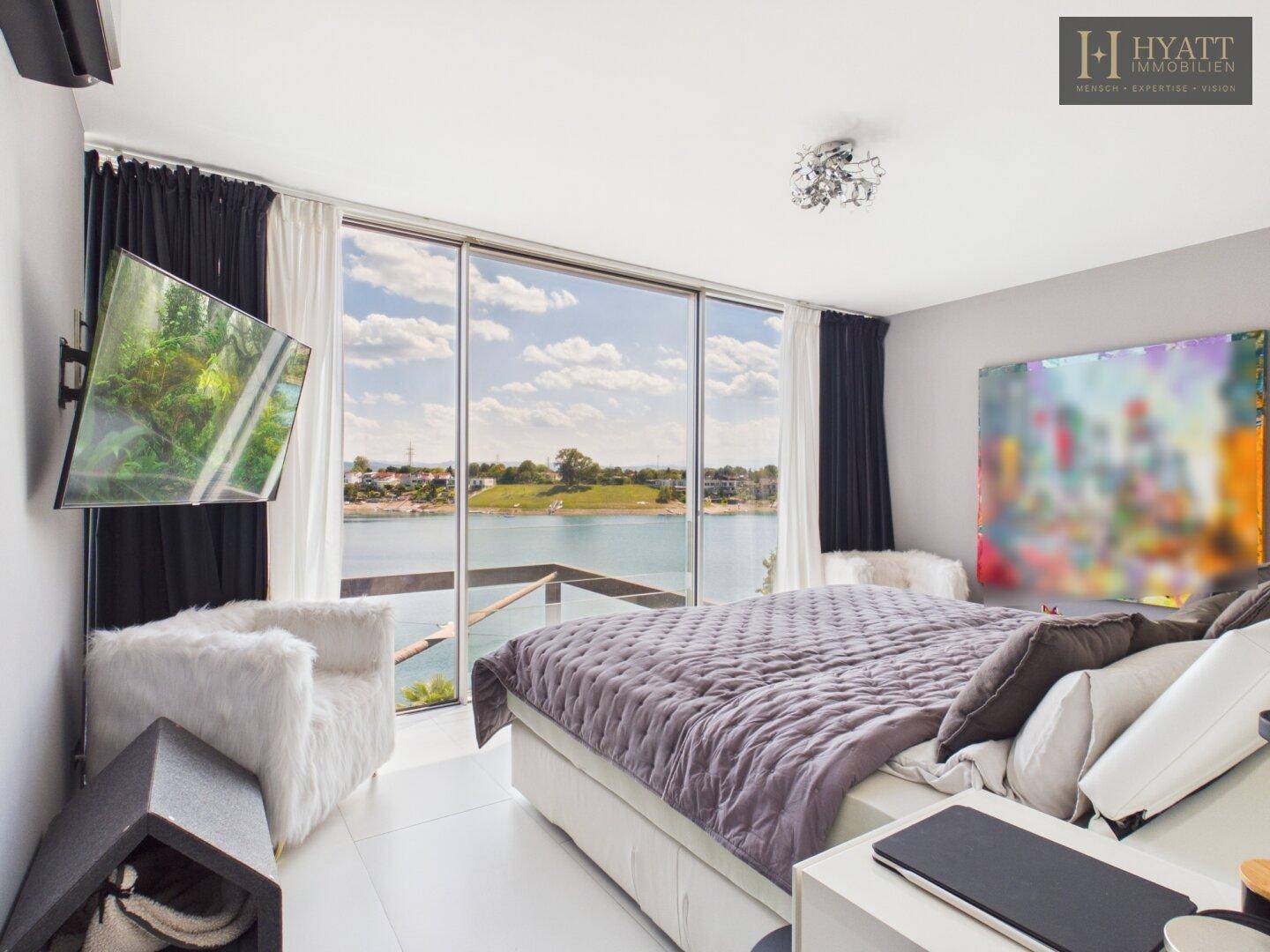 Modernes Schlafzimmer mit raumhohen Fenstern und direktem Blick auf den See.
