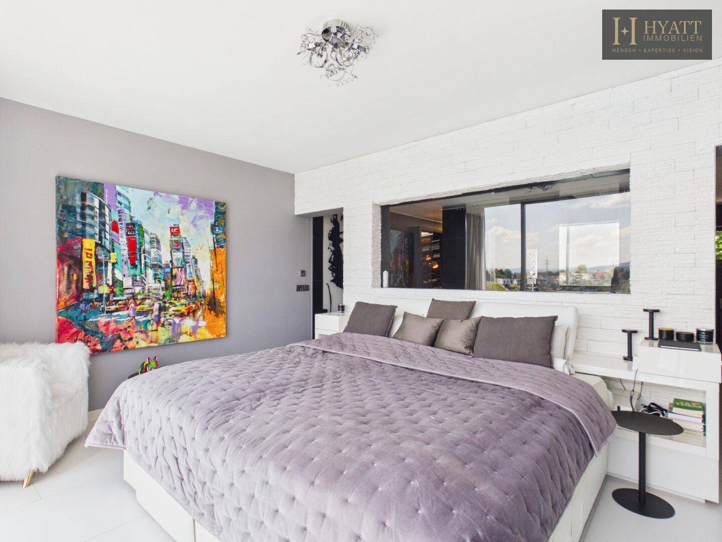 Helles Schlafzimmer mit modernem Bett, Kunstwerken und einer dekorativen Ziegelwand.