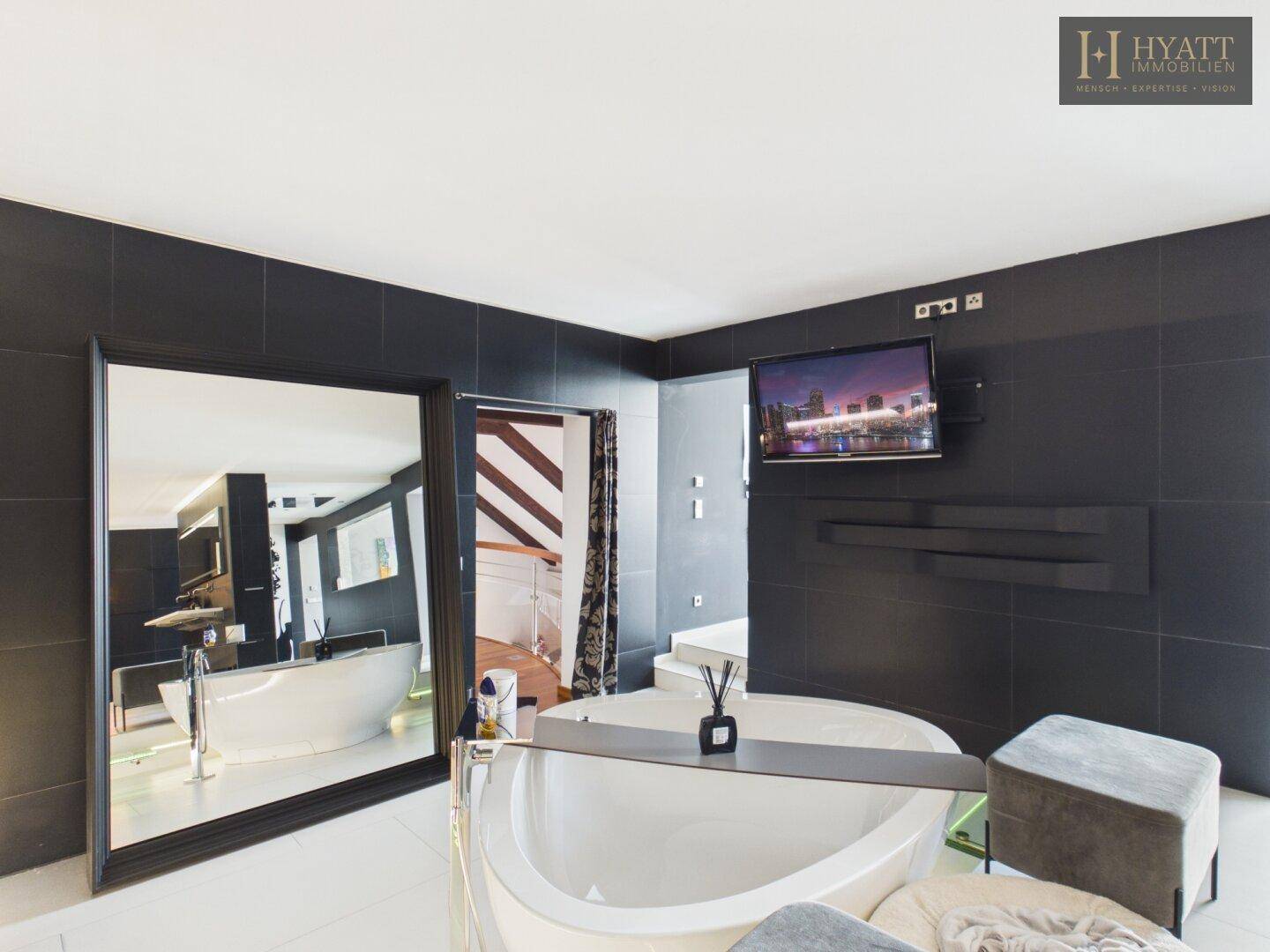 Großzügiges Badezimmer mit freistehender Badewanne, Fernseher und Blick auf den Kleiderschrank.