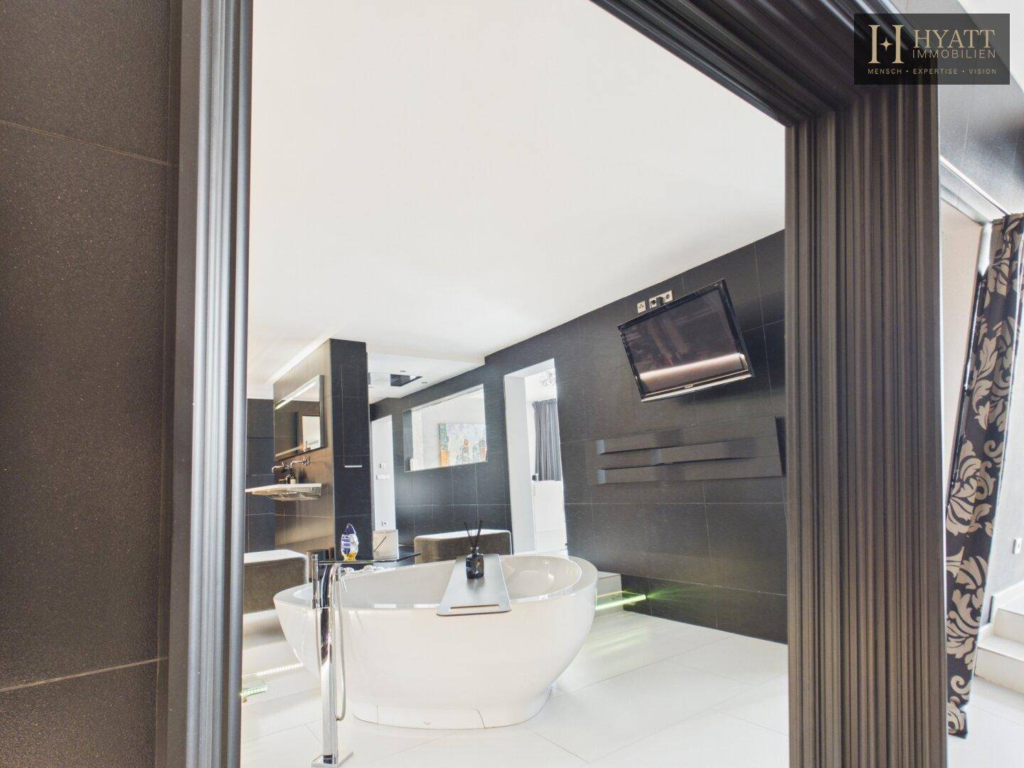 Eingangsbereich zum luxuriösen Badezimmer mit freistehender Badewanne und dunklen Fliesen.