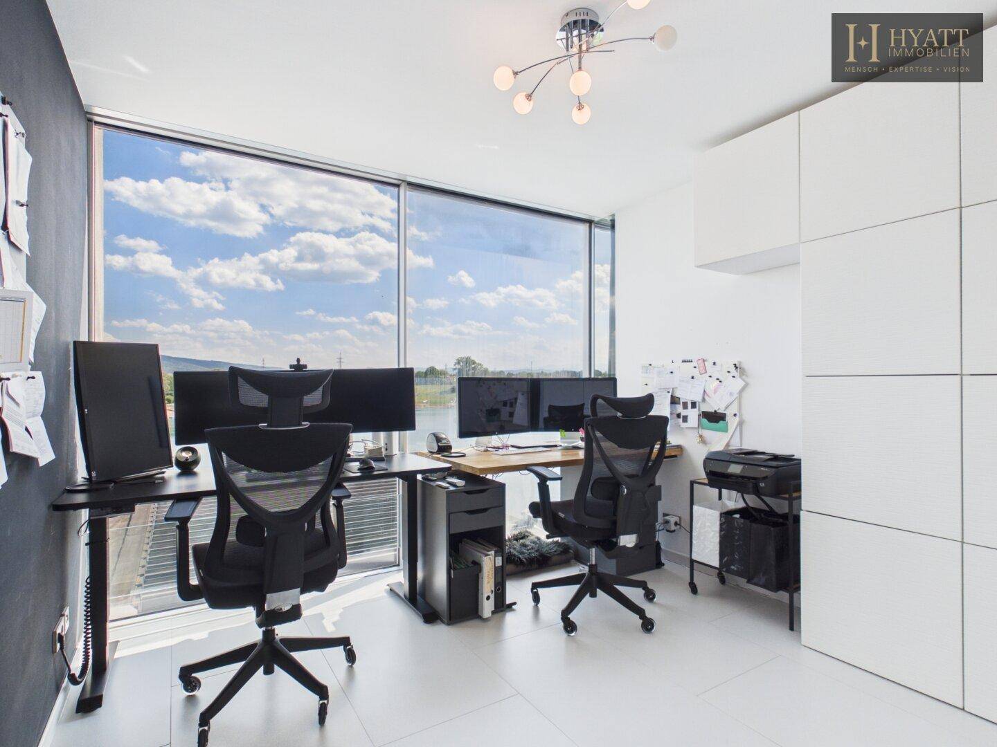 Modernes Heimbüro mit großen Fenstern und inspirierendem Blick auf den See.