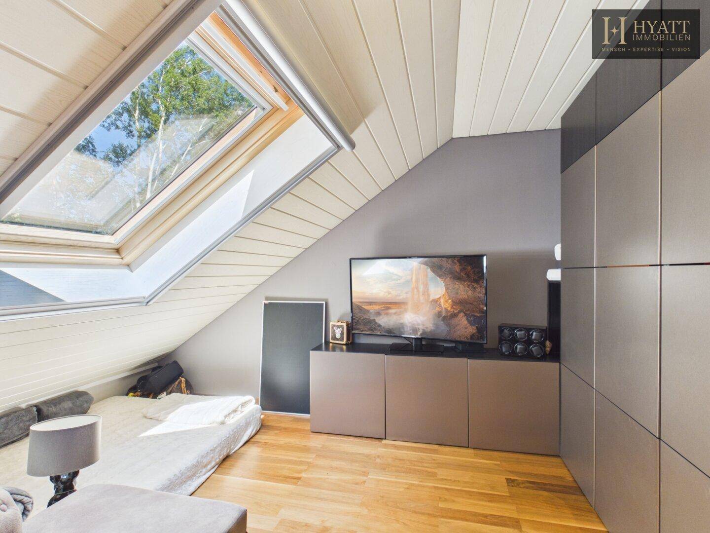 Helles Schlafzimmer im Dachgeschoss mit Dachfenster, Holzboden und integrierten Schränken.