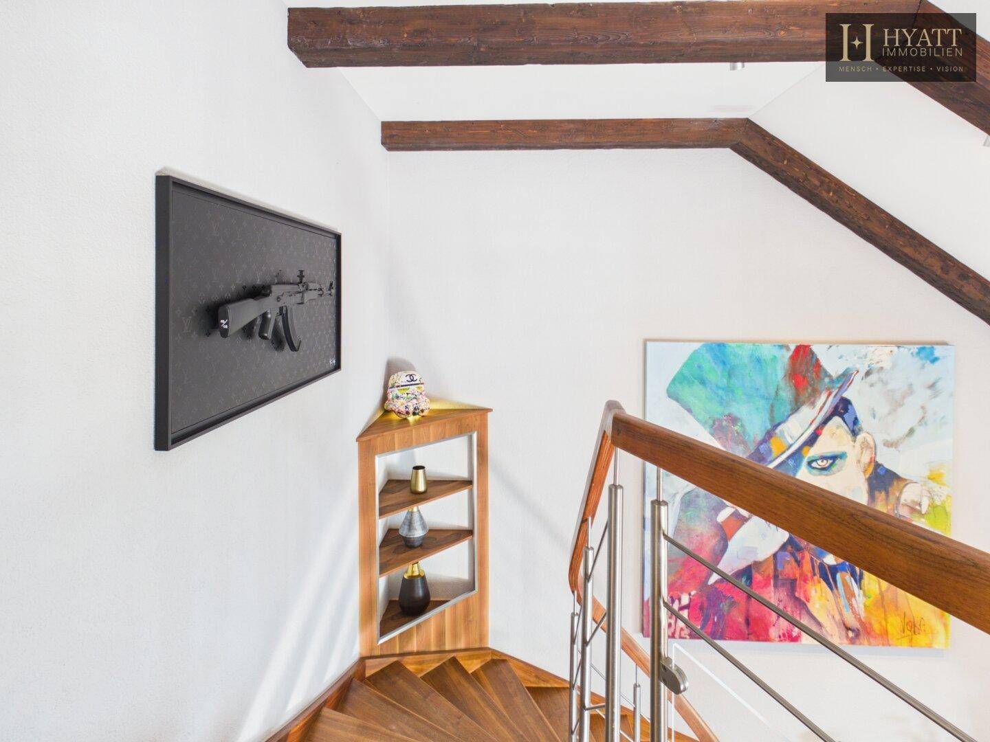 Holztreppe mit Edelstahlgeländer, Kunstwerken und sichtbaren Holzbalken im Treppenhaus.