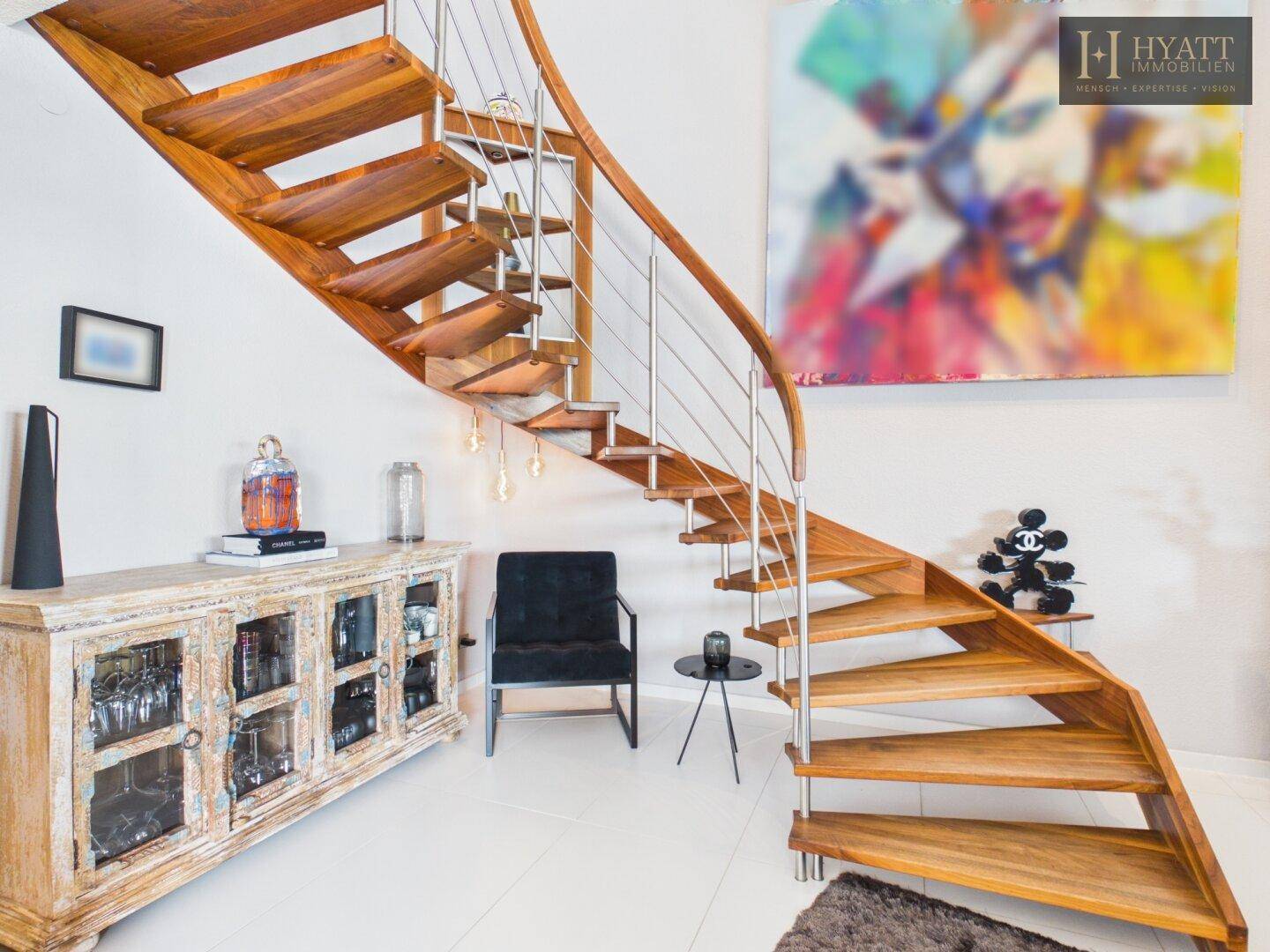Elegante Holzwendeltreppe mit Edelstahlgeländer in einem hellen Eingangsbereich.