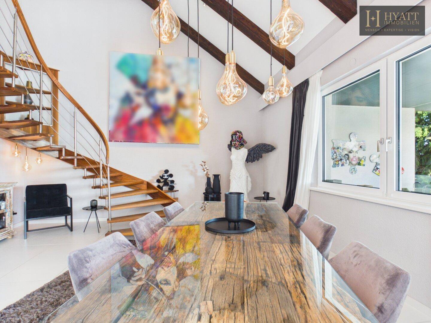 Heller Essbereich mit Holztisch, freiliegenden Deckenbalken und einer eleganten Holztreppe.
