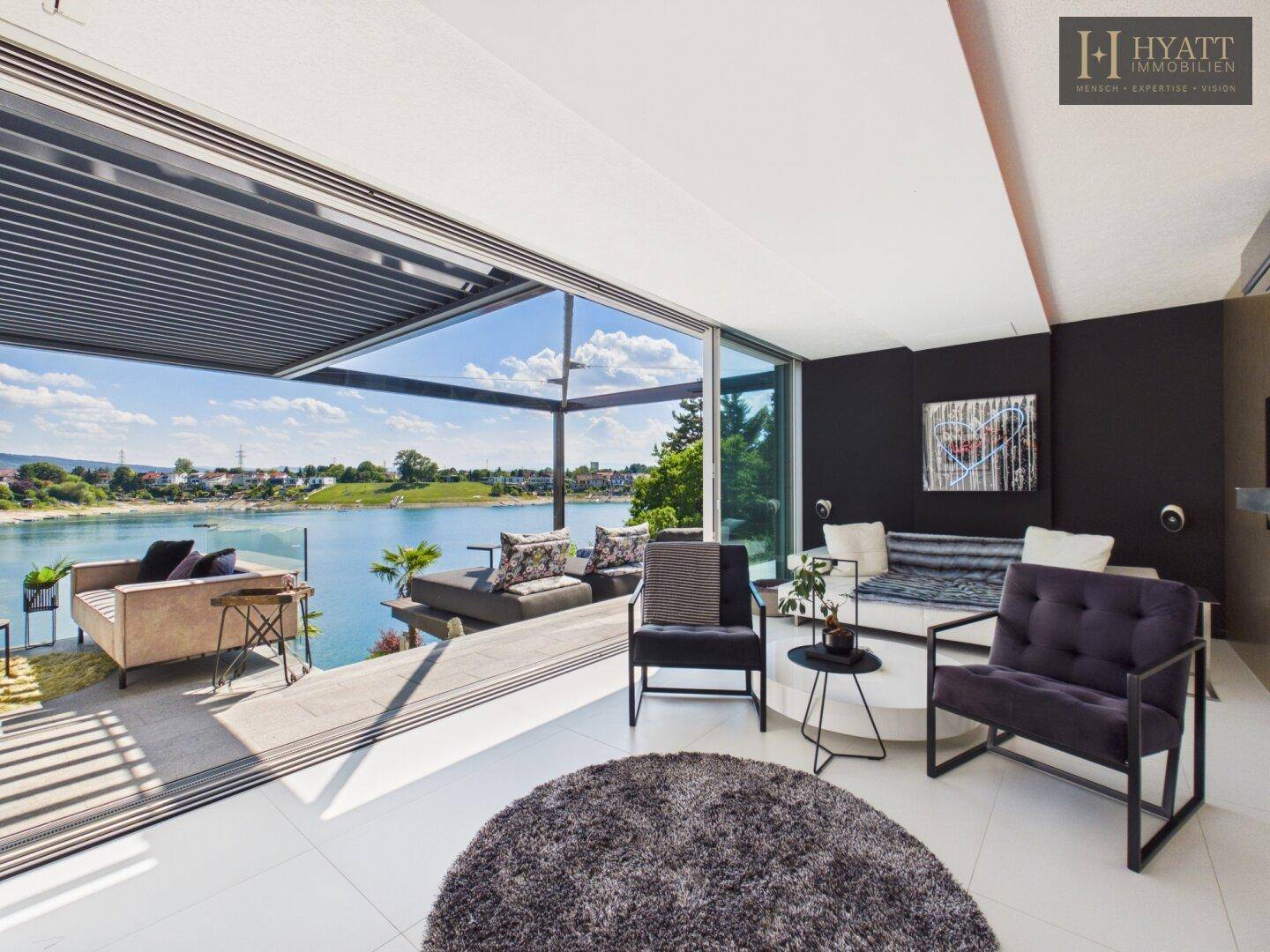 Modernes Wohnzimmer mit großen Glasfronten, die einen weiten Blick auf den See und die Terrasse bieten.