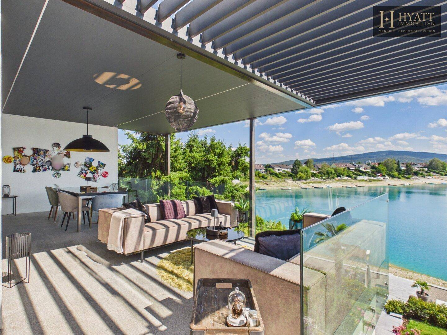 Große überdachte Terrasse mit bequemen Sofas, Esstisch und atemberaubendem Seeblick.
