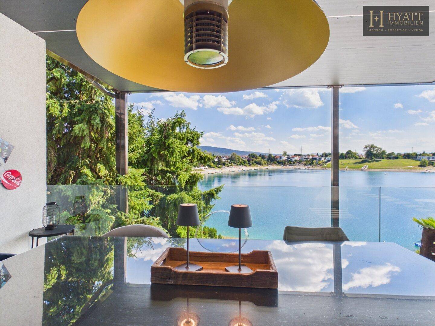 Detailaufnahme des Esstisches auf der Terrasse mit Spiegelung des Himmels und Seeblick.