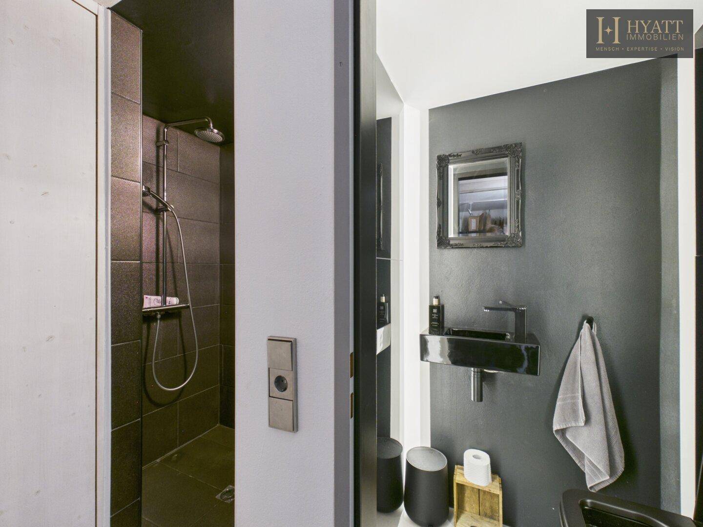 Modernes Gäste-WC mit dunklen Fliesen, Dusche und minimalistischem schwarzen Waschbecken.