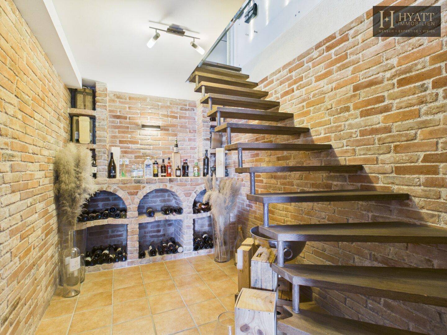Rustikaler Weinkeller mit Ziegelwänden, Weinregalen und einer freischwebenden Holztreppe.