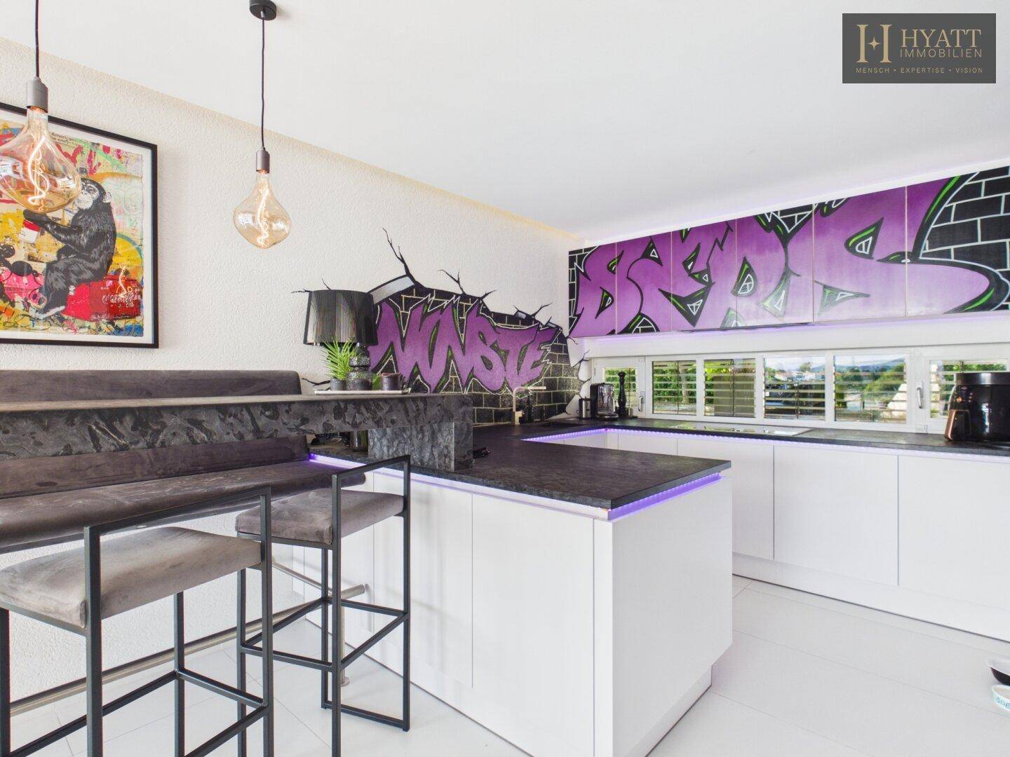 Moderne Küche mit weißen Schränken, einer Kücheninsel und auffälliger Graffiti-Wandgestaltung.