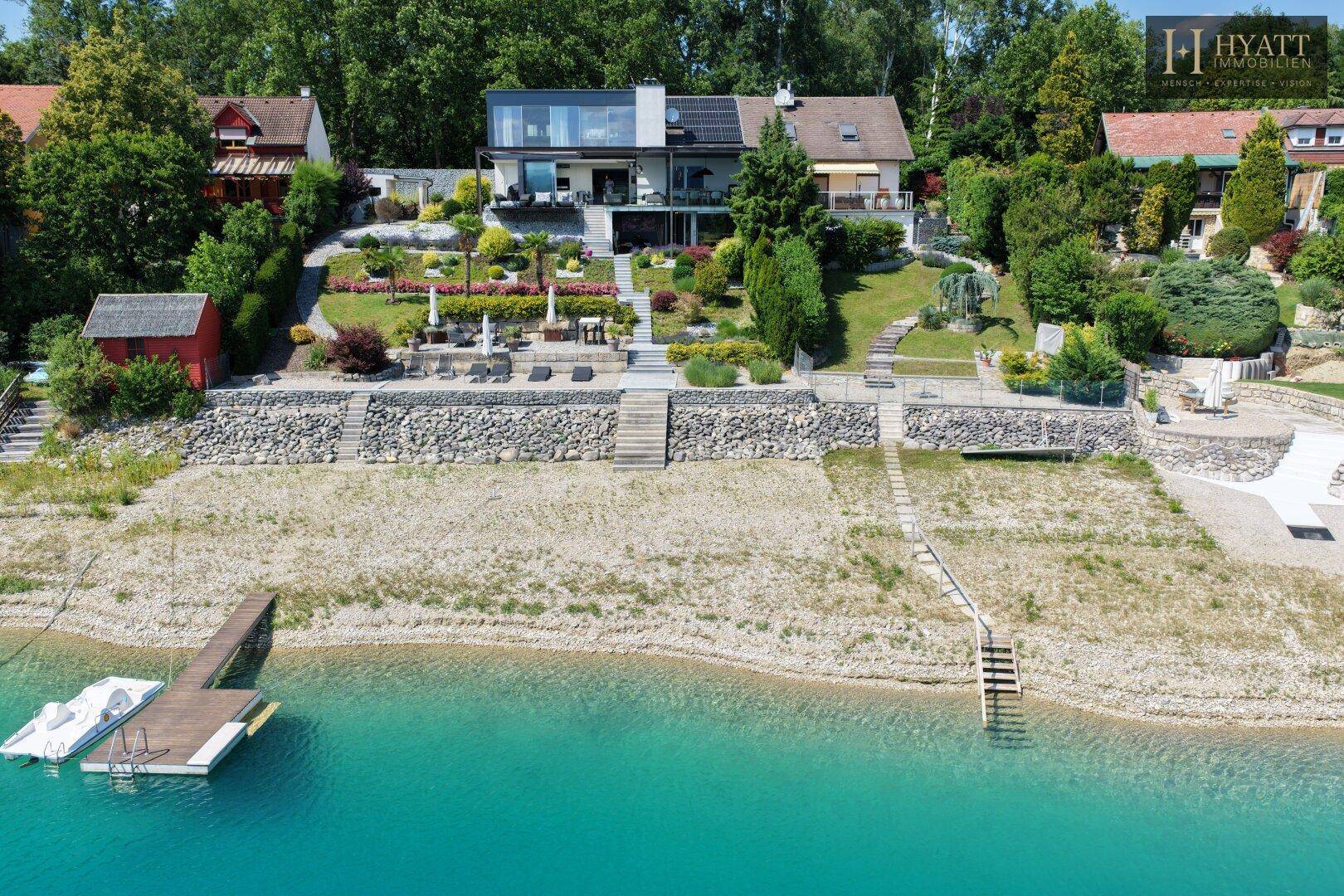 Luftaufnahme einer luxuriösen Villa mit weitläufigem Garten und privatem Seezugang mit Steg.