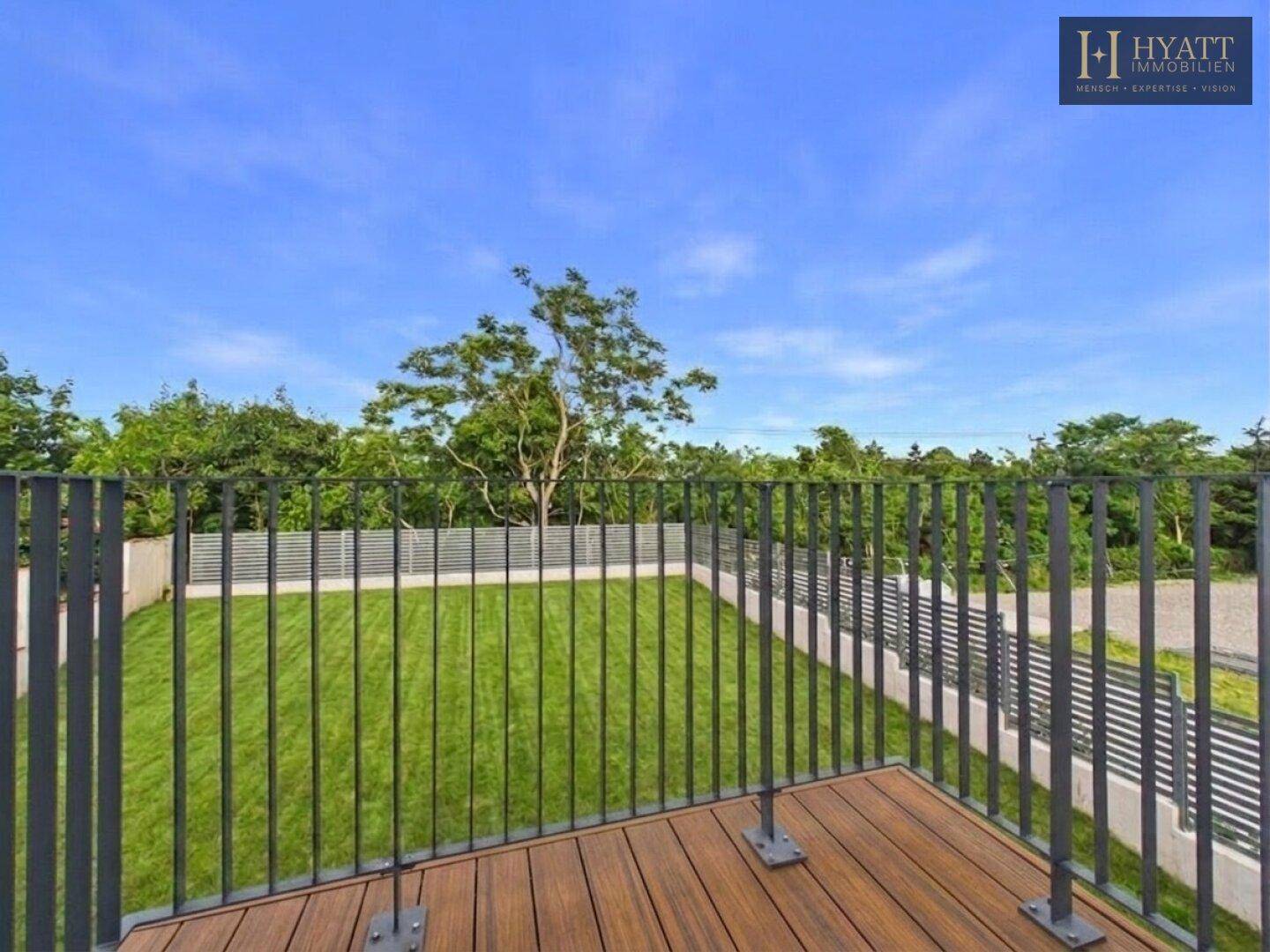 Blick vom Balkon auf den weitläufigen grünen Garten und die umliegende Natur.